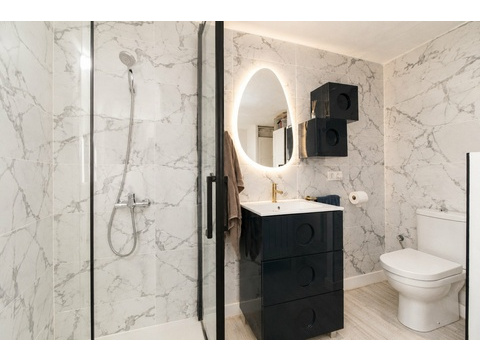 Edles Badezimmer mit Marmor-Fliesenverkleidung, bodengleicher Dusche und beleuchteter Spiegelwand